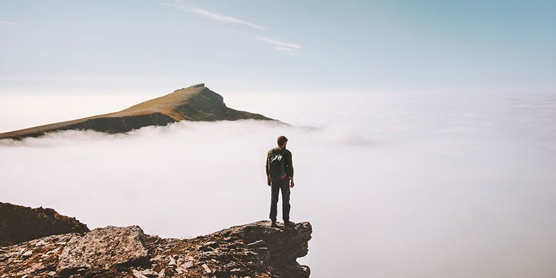person standing on cliff with clouds below